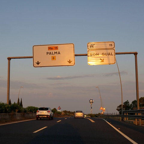 Auf einer Autobahn hängen Schilder mit der Aufschrift "Palma" und "Son Gual", darunter fahren Autos.