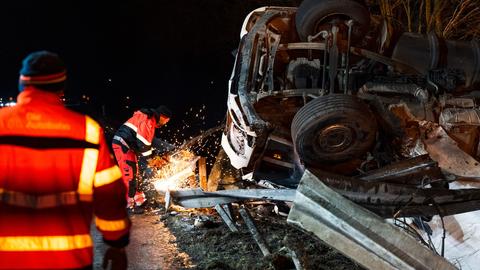 Ein Mann zersägt eine Leitplanke, daneben ein umgekippter Lkw