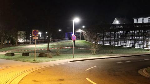 Absperrbänder begrenzen den Tatort auf einer durch eine Straßenlaterne beleuchteten Wiese. Im Hintergrund der nächtlichen Aufnahme ist ein Parkhaus zu sehen. 