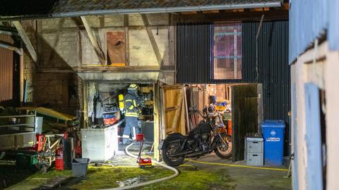 Feuerwehrmann in Scheune, darin verrußt, daneben steht ein Motorrad, es ist Nacht