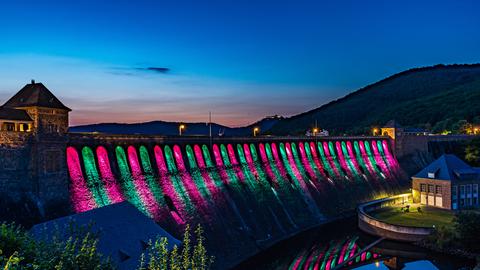 Rosa und Grün beleuchtete Staumauer am Edersee vor im Abendlicht dämmerndem Himmel