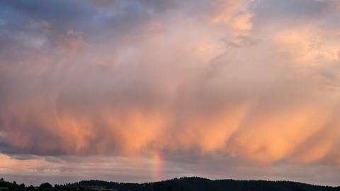 Wolkenreicher Himmel mit kleinem Regenbogen zur Erde