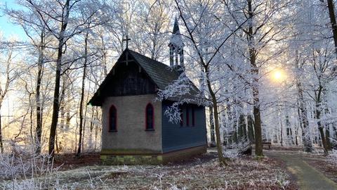 Eine Kapelle umgeben von Bäumen und Sträuchern, die mit Raureif bedeckt sind.