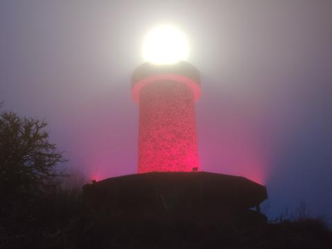 Rot angestrahlter Turm mit stark leuchtender Lampe auf der Spitze in der Dunkelheit