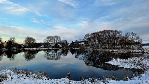 Um einen See liegt Schnee, der Himmel dahinter ist blau