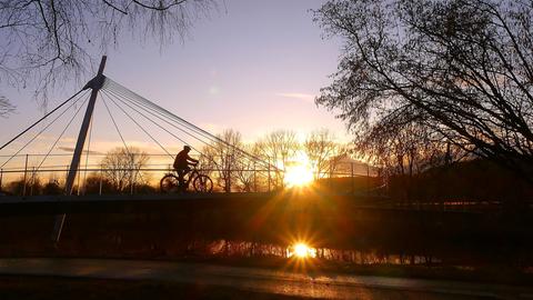 Radfahrer fährt über Brücke, hinter ihm die untergehende Sonne