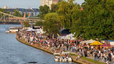 Am Mainufer in Frankfurt sind Besucherinnen und Besucher eines Festes zwischen Essensständen unterwegs.