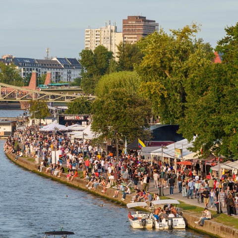 Am Mainufer in Frankfurt sind Besucherinnen und Besucher eines Festes zwischen Essensständen unterwegs.