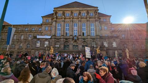 Dutzende Demoteilnehmer stehen vor dem kasseler rathaus, die sonne blitzt über das Gebäude, der Himmel ist blau