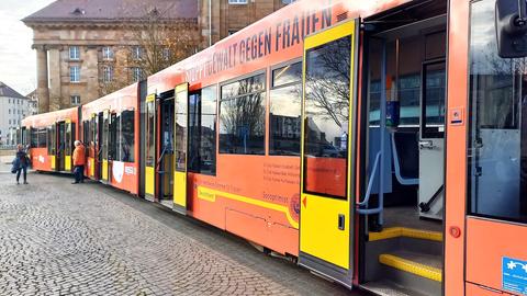 Eine Straßenbahn der KVG ist orange beklebt. Der Schriftzug "Stop gegen Gewalt an Frauen" steht in mehreren Sprachen darauf.