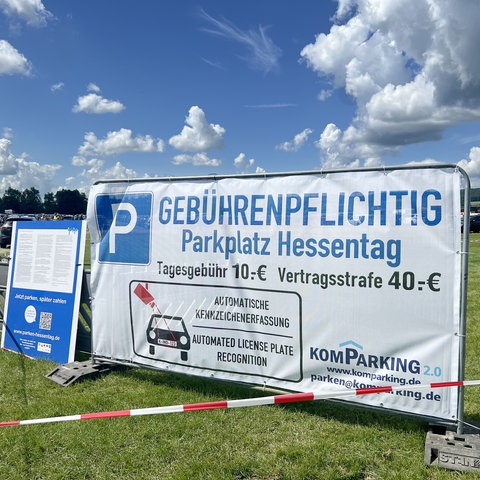 Ein Banner hängt an einem Metallzaun. Darauf steht: Gebührenpflichtig. Parkplatz Hessentag. Tagesgebühr: 10 Euro. Vertragsstrafe: 40 Euro.