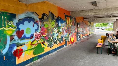 Im Laubengang des Frankenberger Parkhauses haben Jugendliche bunte Graffiti an die Wände gesprüht. Zu sehen sind großflächige Schriftzüge, ein Teddybär, eine Katze und mehrere Herzen.