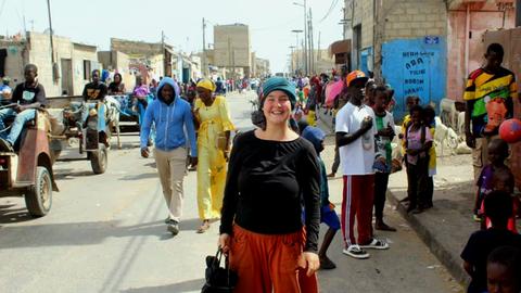 Charlotte steht auf einer Straße im Senegal - im Hintergrund Pferdekutschen. 