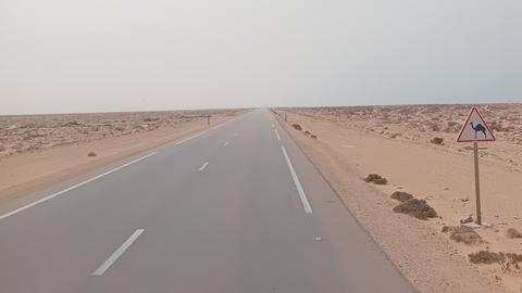 Eine Straße in der Wüste mit einem "Achtung-Kamele-Schild"