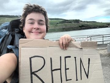 Claudi mit einem Pappschild mit der Aufschrift "Rhein".