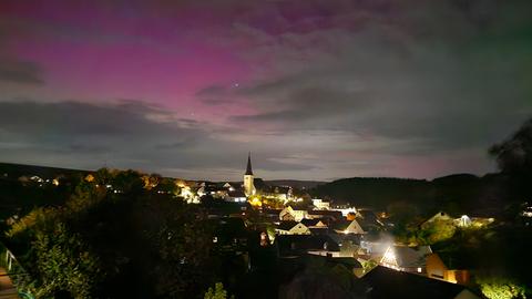 Rosa gefärbter Nachthimmel über einer Stadt mit erleuchteter Kirche