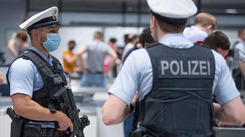 Polizisten stehen mit Maske und Pistolen in der Wartehalle des Flughafens. 