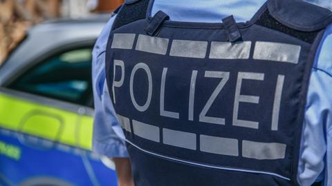 Rücken von Polizist mit Aufschrift "Polizei" - Polizeiauto im Hintergrund