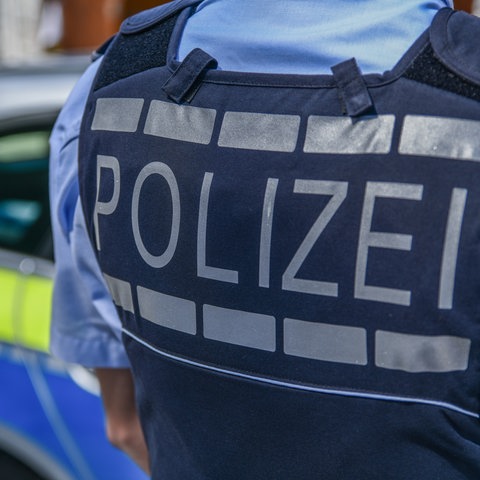 Rücken von Polizist mit Aufschrift "Polizei" - Polizeiauto im Hintergrund