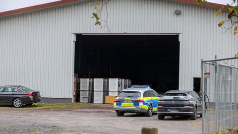 Ein Polizeiwagen steht zwischen zwei anderen Autos vor einer geöffneten Lagerhalle.