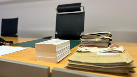 Ein Tisch, hinter dem ein schwarzer Bürostuhl steht. Auf dem Tisch liegen Aktenordner und Gesetzesbücher.