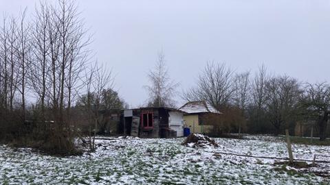 Eine verlassene Gartenhütte. Die Tür steht offen. Der Kleingarten ist sehr ungepflegt.