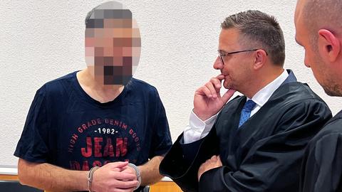 Zwei Anwälte und ein Angeklagter (Gesicht verpixelt) im Gespräch miteinander