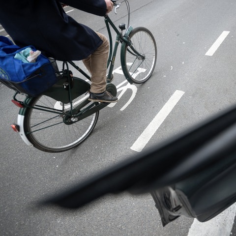 Ein Fahrradfahrer fährt an einer geöffneten Autotür vorbei.