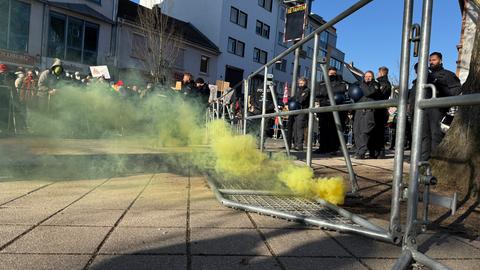 Gelber Rauch quillt aus einer Rauchbombe, die an einem Absperrgitter liegt, dahinter auf der einen Seite Polizisten, auf der anderen Demonstrierende