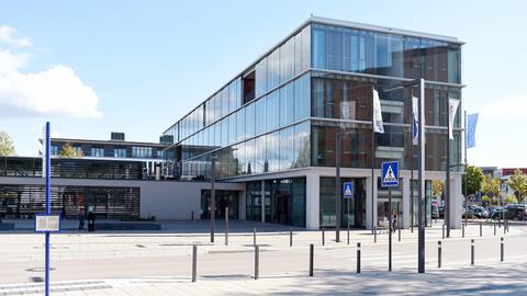 Zeitgenössiches Gebäude mit Glasfassade, auf einem Platz mit Straße und Bushaltestelle stehend.