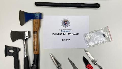 Auf einem Tisch liegen Messer, Äxte und mehrere Schlagstöcke. Auf einem Zettel ist das Logo der Hessischen Polizei zu sehen.