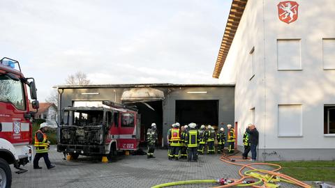 Feuerwehrleute stehen neben dem verbrannten Einsatzfahrzeug in der Einfahrt zur Feuerwehrhalle.