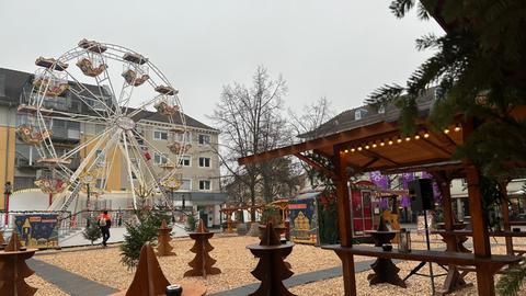 Rostrote Stehtische in Form eines Tannenbaums vor einem kleinen Kinderriesenrad. Nur ein Mensch mit rotem Anorak und Rucksack läuft hinten durchs Bild.