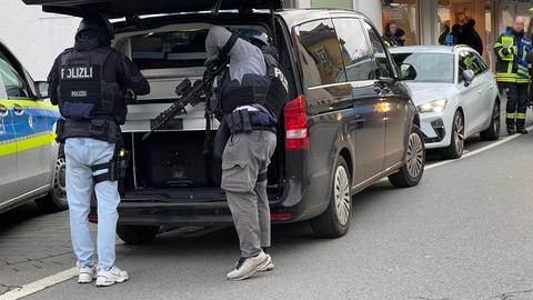 Ein Polizist mit Waffe, sucht etwas in einem schwarzen Polizeiauto.