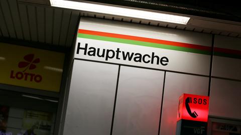 In einer S-Bahn-Station steht auf einer Wand von oben beleuchtet "Hauptwache". Darunter leuchtet eine SOS-Säule rot. Links daneben ein Laden mir gelber Werbung "Lotto".