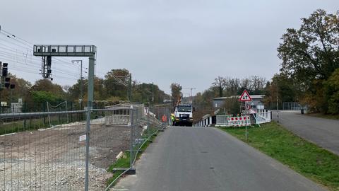 Rodungsarbeiten entlang einer Bahnstrecke - Gleisbereich - gerodete Fläche - ein Bauzaun. Auf einer Zugangsstraße, die parallel zu den Gleisen verläuft, steht ein Lkw - Bauarbeiter daneben. 