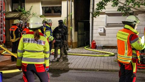 Einsatzkräfte von Feuerwehr und Polizei stehen in der Straße vor einem künstloch beleuchteten Haus.