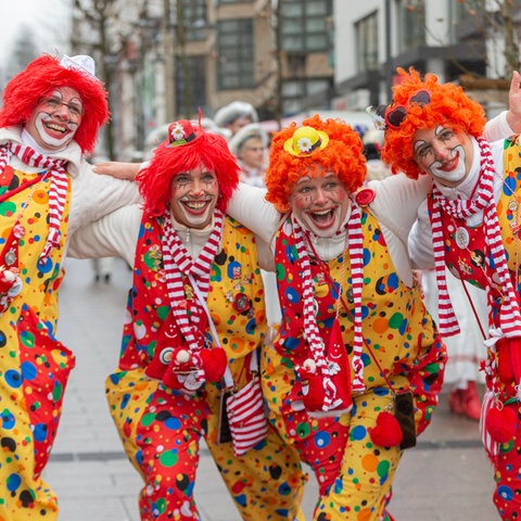 Vier Personen in Clownskostümen stehen lachend auf einer Straße.