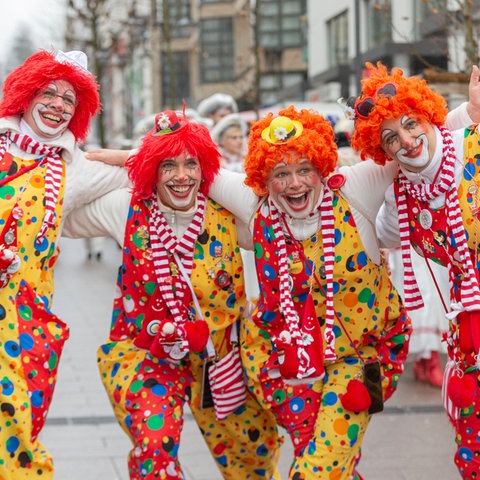 Vier Personen in Clownskostümen stehen lachend auf einer Straße.