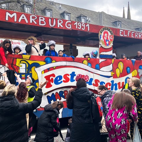 Motivwagen des Elferrats beim Rosenmontagsumzug in Marburg, kostümierte Zuschauer stehen davor