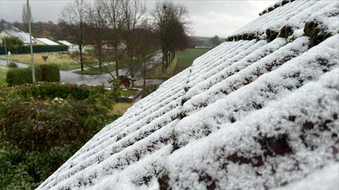 Etwas Schnee liegt auf einem Hausdach.