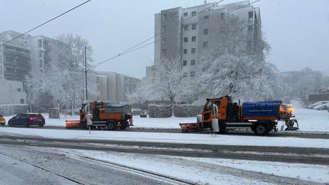 Orangefarbende Räumungsfahrzeuge auf einer verschneiten Straße.