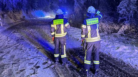 Zwei Feuerwehrmänner stehen nachts vor verschneiten Bäumen