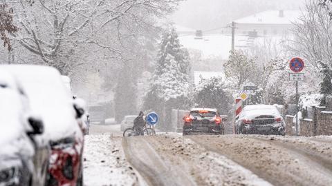 Eingemummter Mann schiebt sein Fahrrad über die mit Schnee bedeckte Straße.