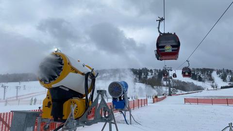 Die Ettelsbergseilbahngondeln fahren neben Schneekanonen, die in Betrieb sind und Pulverschnee produzieren