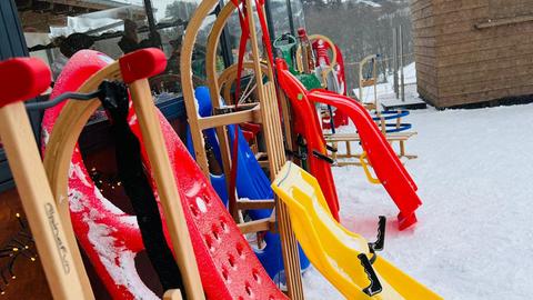 Mehrere gelbe und rote Schlitten aus Holz und Plastik lehnen an einer Wand im Schnee