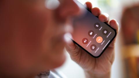 Ein älterer Mann führt ein Telefongespräch am Smartphone. Man sieht ihn unscharf, das Display des Telefons ist scharf. Darauf sieht man einen roten Button zum Auflegen.