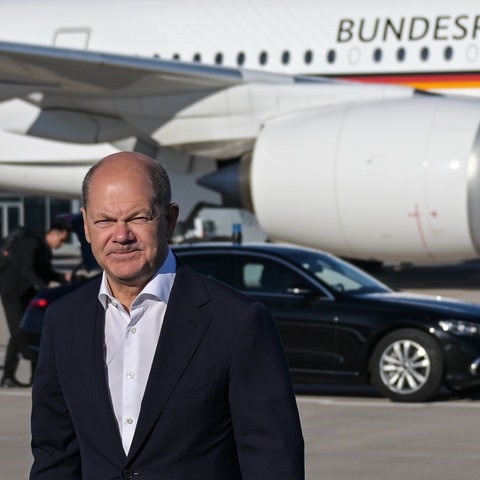 Scholz steht mit verkniffenem Gesichtsausruck vor einem Flugzeug mit Aufdruck Bundesrepublik