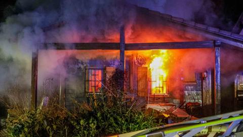 Brennender Flachbau, Flammen schlagen aus einem der zwei Fenster, viel Qualm am Nachthimmel