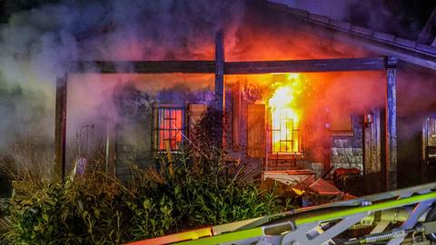 Brennender Flachbau, Flammen schlagen aus einem der zwei Fenster, viel Qualm am Nachthimmel